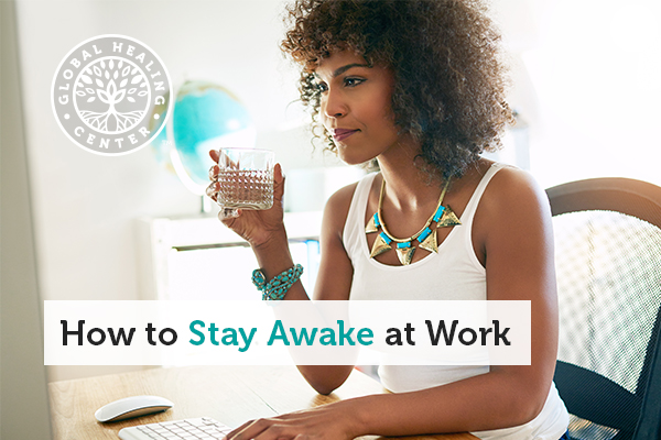 A woman drinking water while working. Maintaining hydrate is key for staying awake at work.