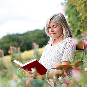 Mature woman sitting in chair and reading a book in flower field. PQQ: An Essential Nutrient for Healthy Aging & Longevity.